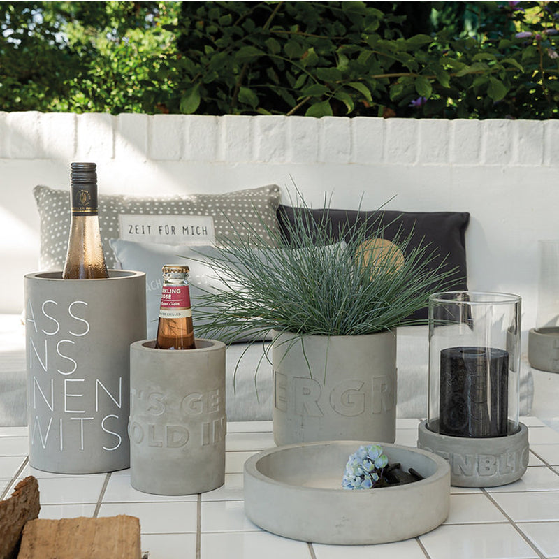 Auch für den Outdoor-Bereich: Beton-Windlicht AUGENBLICK von Räder Design, Sockel aus Beton mit Relief, Zylinder aus klarem Glas, kombiniert mit Flaschenkühler

