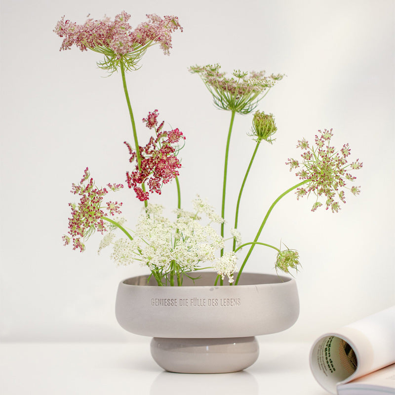 Diese Steingut-Schale in der Farbe Grau mit dem Schriftzug "Genieße die Fülle des Lebens", mit einem kleinen Standfuß, und der Form von Kieselsteinen, ist besonders schön mit einem Trockenblumen-Gesteck.  Sie ist von Räder-Design und im Online-Shop Home-and-Kitchen zu bestellen.