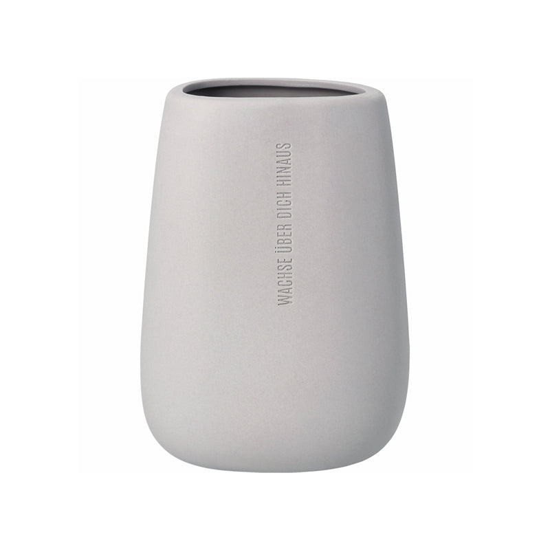 Die Räder Design Steingut-Vase "Wachse über dich hinaus", wurde in Kieselstein-Form gestaltet und auf der matten Außenseite mit dem Schriftzug versehen. Ihr Inneres ist glasiert und ebenso der Deckel, der ein kleines Loch für einzelne Blumenstängel hat. Ihre Größe beträgt 10,3x8,4x17,4 cm